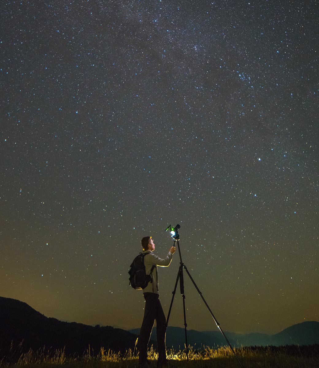 The man with a camera stand on the starry sky background. night time.