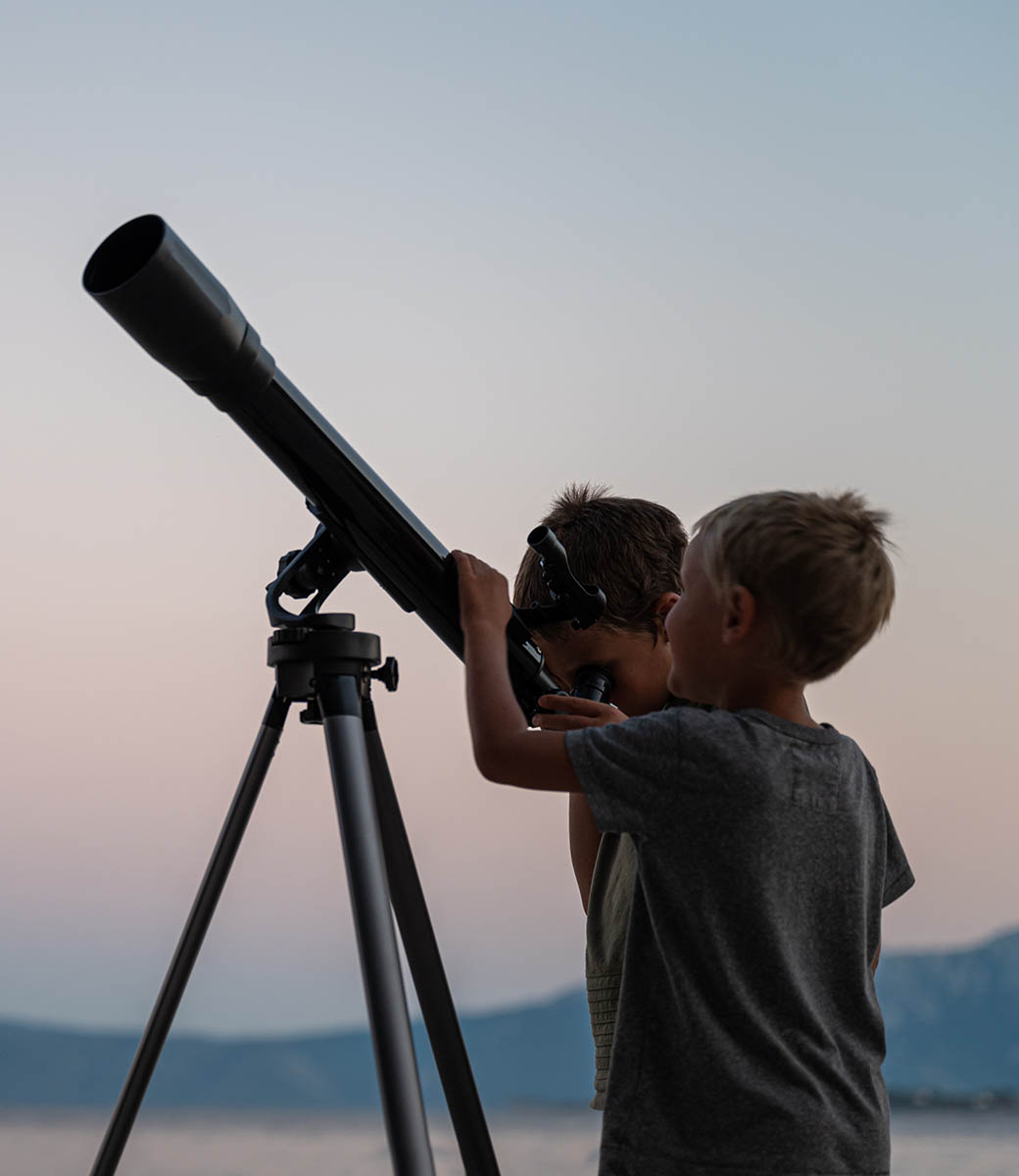 Two brothers looking at the stars using a telescope by the sea