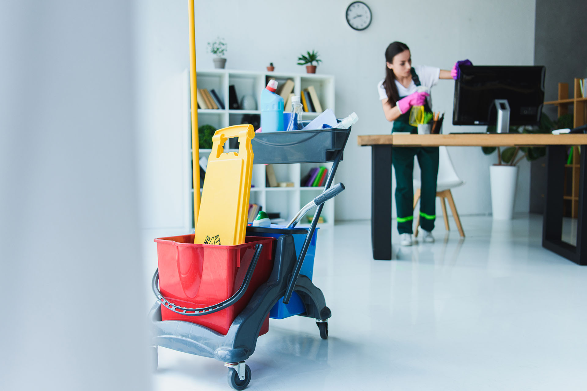 young female janitor cleaning office with various cleaning equip